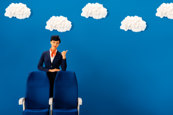 усміхнений афроамериканський стюардеса, що показує як біля сидіння на синьому фоні з хмарами
  - Фото, зображення