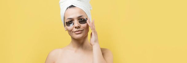 Young beautiful girl in a white towel on his head wears collagen gel patches under her eyes. Mask under eyes treatment face. - Foto, Bild