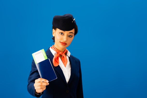 Afrikaans-Amerikaanse stewardess met paspoort en vliegticket geïsoleerd op blauw  - Foto, afbeelding
