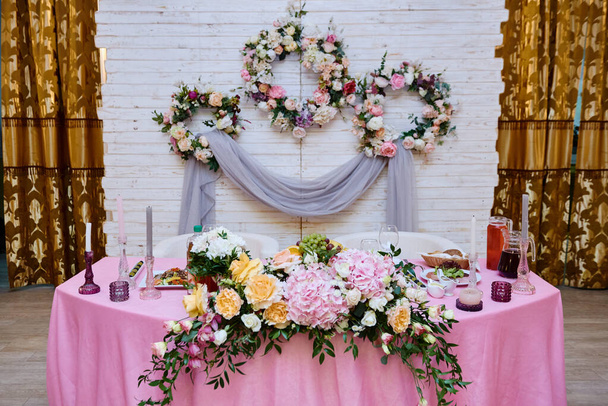 Wedding presidium in restaurant, copy space. Banquet table for newlyweds with flowers, greenery, candles and pink cloth. Lush floral arrangement. Luxury wedding decor - Photo, image
