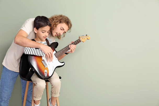 Ο άντρας μαθαίνει στο γιο του να παίζει κιθάρα σε έγχρωμο φόντο. - Φωτογραφία, εικόνα
