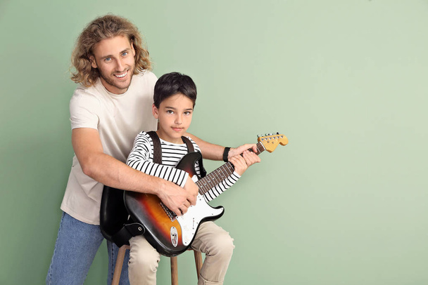 Man teaching his son to play guitar on color background - Fotoğraf, Görsel