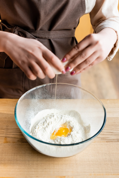 rajattu näkymä nainen lisäämällä raaka muna kulhoon jauhoja
  - Valokuva, kuva