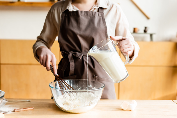 vista cortada de mulher derramando leite em tigela com farinha
  - Foto, Imagem
