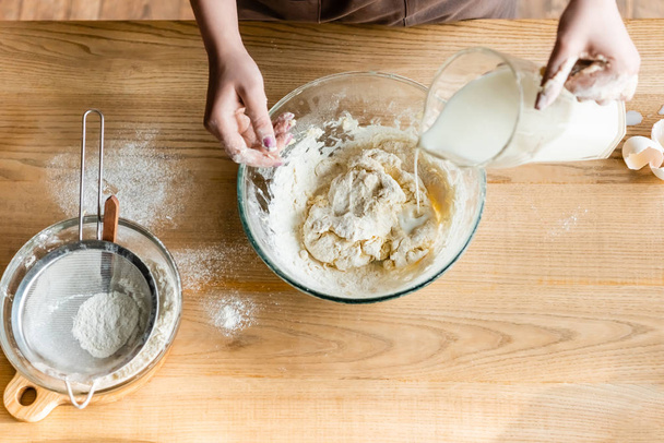 top view of woman pouring milk in bowl with dough  - Photo, Image