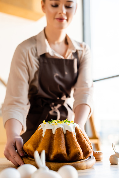 foco seletivo da mulher segurando bolo de Páscoa perto de estatuetas com coelhos decorativos
  - Foto, Imagem