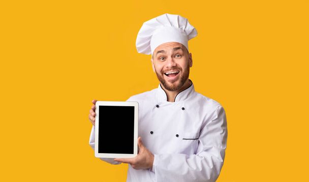 Happy Chef Showing Digital Tablet Screen On Yellow Studio Background - Photo, Image