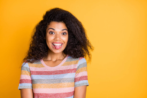 Close-up portrait of her nice attractive funky cheerful cheery girlish wavy-haired girl in striped t-shirt showing tongue out having fun isolated on bright vivid shine vibrant yellow color background - Foto, Bild