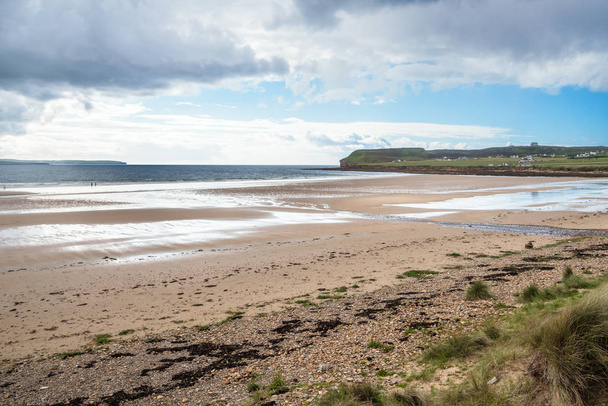 Kaunis suuri ranta laskuveden aikaan osittain pilvisenä kevätpäivänä. Kaksi ihmistä koiran kanssa kävelemässä rannalla ovat näkyvissä etäisyydellä. Thurso, Skotlanti, Yhdistynyt kuningaskunta
. - Valokuva, kuva