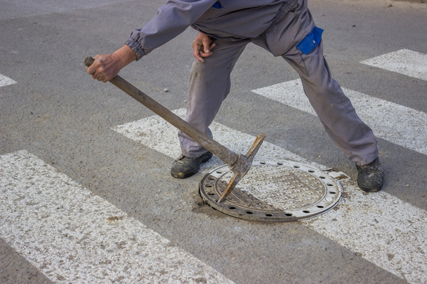 Utilitários trabalhador move a tampa do bueiro
 - Foto, Imagem