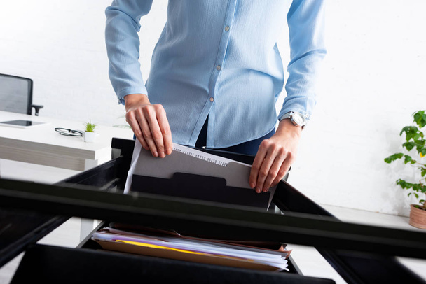 Cropped view of businesswoman taking folder with dossier from open cabinet driver in office - 写真・画像