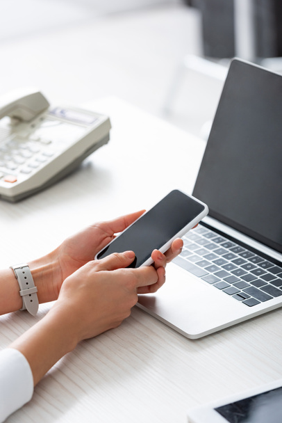 Обрізаний вид бізнес-леді, використовуючи смартфон біля ноутбука та цифрового планшета на столі
 - Фото, зображення