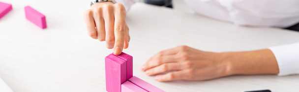 Cropped view of businesswoman stacking pink building blocks on table, panoramic shot - Photo, image