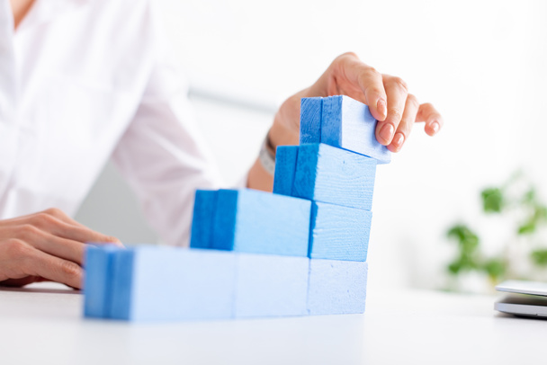 Selective focus of businesswoman making marketing pyramid with blue building blocks near laptop on table - Zdjęcie, obraz