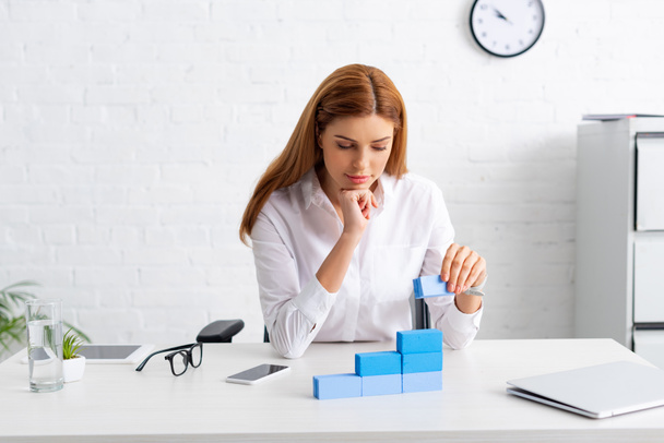 Attraktive Geschäftsfrau stapelt Marketingpyramide aus blauen Bausteinen auf Tisch - Foto, Bild