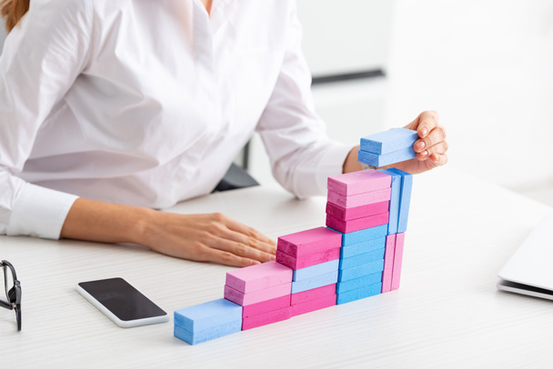 Gewassen beeld van zakenvrouw stapelen marketing piramide van bouwstenen op tafel - Foto, afbeelding
