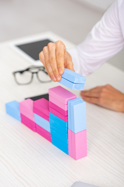 Cropped view of businesswoman making marketing pyramid from colorful building blocks on table - Photo, image