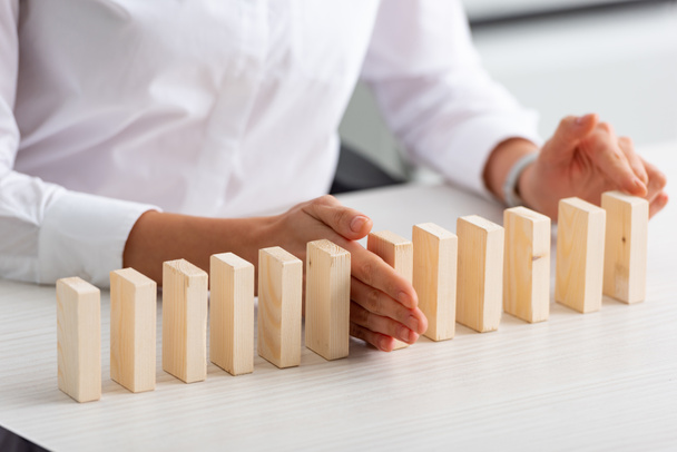 Cropped view of businesswoman holding wooden building blocks on table - Fotoğraf, Görsel