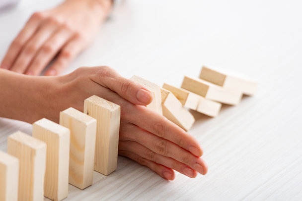 Cropped with of businesswoman holding falling building blocks with hand on table on white background - Fotoğraf, Görsel
