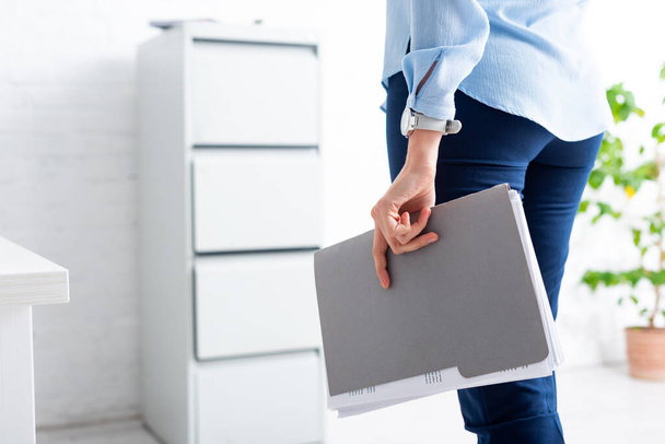 Обрезанный вид деловой женщины, держащей папку с досье в офисе
 - Фото, изображение