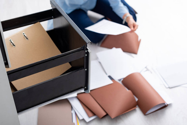 Selective focus of businesswoman with documents near open cabinet driver sitting on floor - Photo, Image