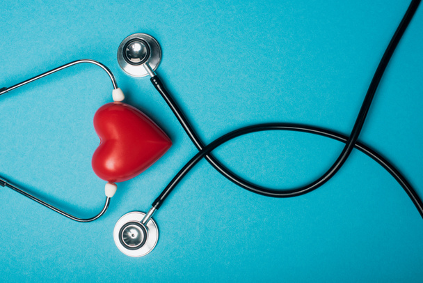 Horní pohled na dekorativní červené srdce a černý stetoskop na modrém pozadí, koncept světového dne zdraví - Fotografie, Obrázek