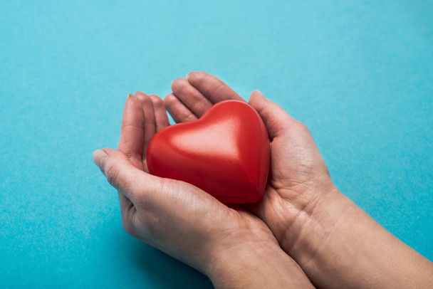 Vista cortada de coração vermelho decorativo em mãos de mulher no fundo azul, conceito de dia de saúde mundial
 - Foto, Imagem