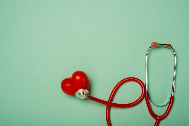 Top view of stethoscope connected with decorative red heart on green background, world health day concept - Photo, Image