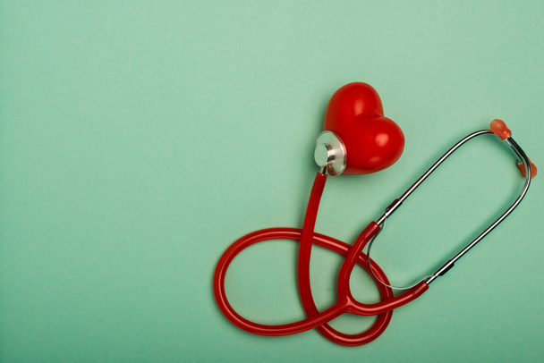 Top view of red stethoscope connected with decorative heart on green background, world health day concept - Фото, изображение