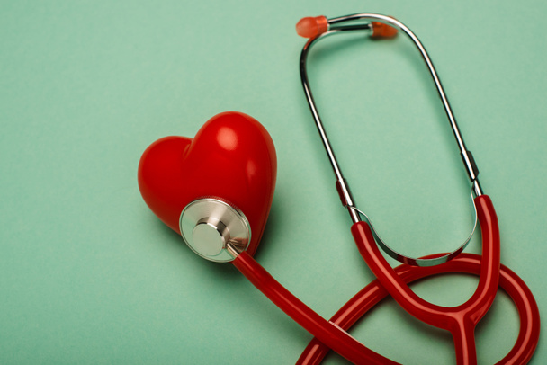 Red stethoscope connected with decorative heart on green background, world health day concept - 写真・画像