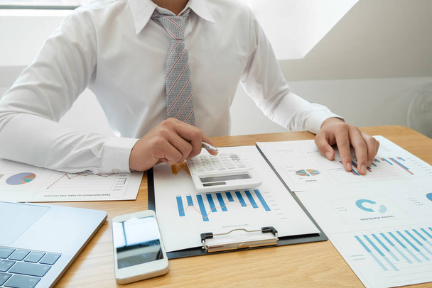 Egy üzletember ül az asztalnál, és számolgatja a pénzügyi grafikonokat az ingatlanbefektetési kiadásokról. - Fotó, kép