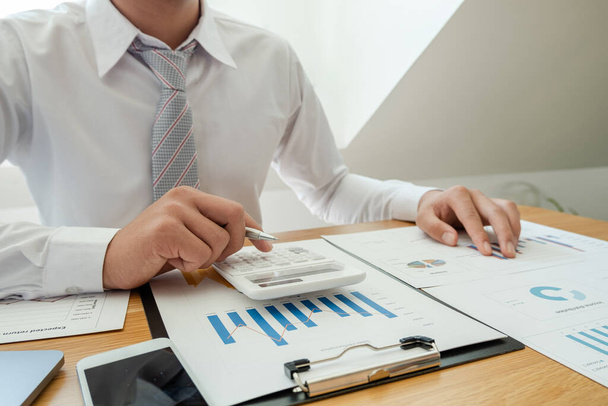 Egy üzletember ül az asztalnál, és számolgatja a pénzügyi grafikonokat az ingatlanbefektetési kiadásokról. - Fotó, kép