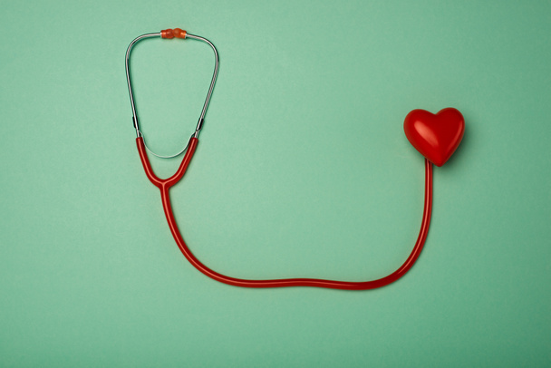 Draufsicht auf Stethoskop und dekoratives rotes Herz auf grünem Hintergrund, Konzept zum Weltgesundheitstag - Foto, Bild