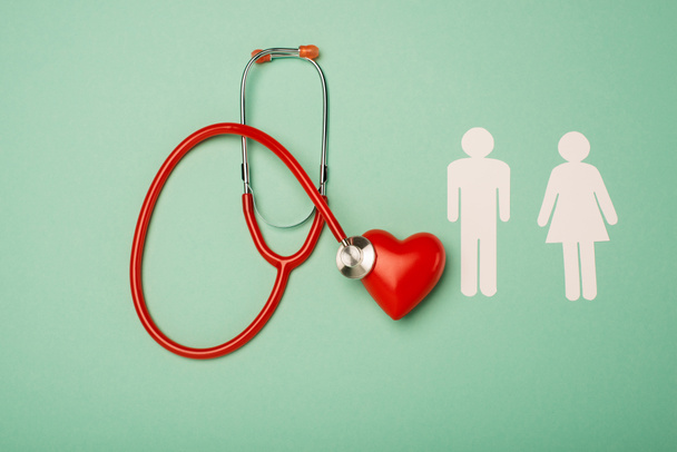 Top view of stethoscope, red heart with male and female icons on green background, world health day concept - Photo, Image