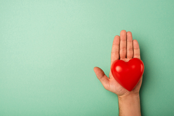 Top view of decorative red heart in man hand on green background, world health day concept - Foto, Imagen