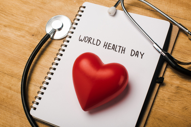 世界の健康の日のレタリングとノートブック上の聴診器、装飾的な赤いハート木製の背景 - 写真・画像