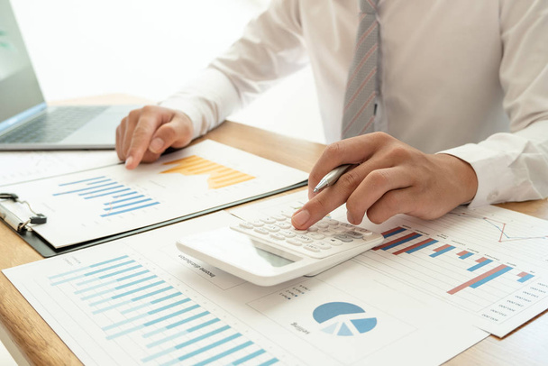 Un hombre de negocios está sentado en un escritorio y calculando gráficos financieros sobre los gastos de inversión inmobiliaria
 - Foto, Imagen