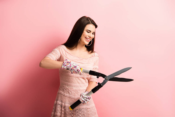 happy girl in working gloves holding gardening scissors on pink background - Photo, Image