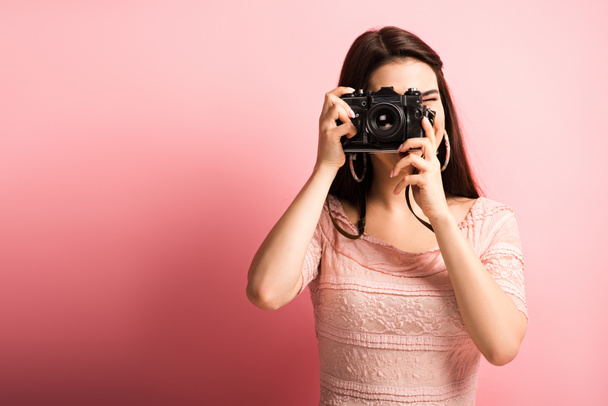 photographer in elegant dress taking photo on digital camera on pink background - Фото, зображення