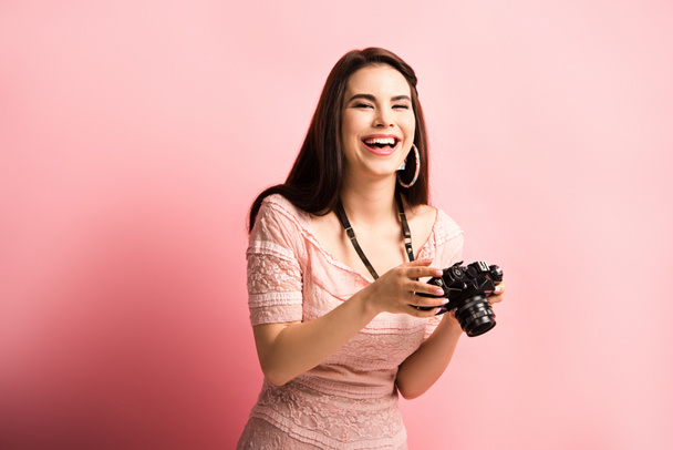 happy photographer laughing while holding digital camera on pink background - Photo, Image