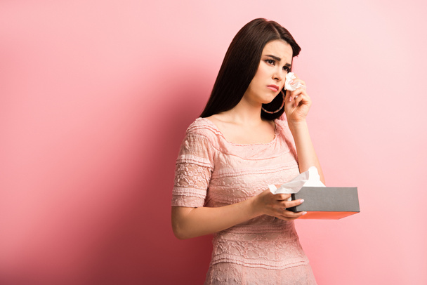 offended girl crying and wiping tears with paper napkin on pink background - Photo, Image