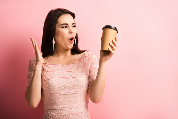 amazed girl showing wow gesture while holding coffee to go on pink background - Foto, immagini