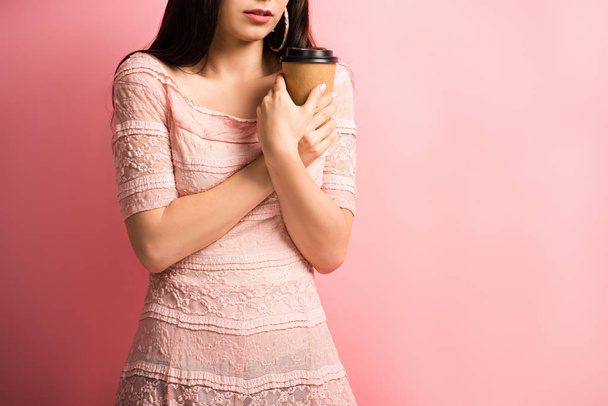 bijgesneden uitzicht van boos meisje houden van koffie te gaan terwijl staan op roze achtergrond - Foto, afbeelding