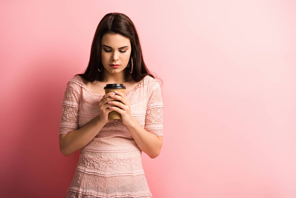 αναστατωμένο κορίτσι κρατώντας καφέ για να πάει, ενώ στέκεται σε ροζ φόντο - Φωτογραφία, εικόνα
