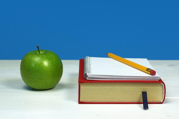 Manzana verde y libro, con cuaderno y lápiz sobre superficie de madera blanca
 - Foto, imagen