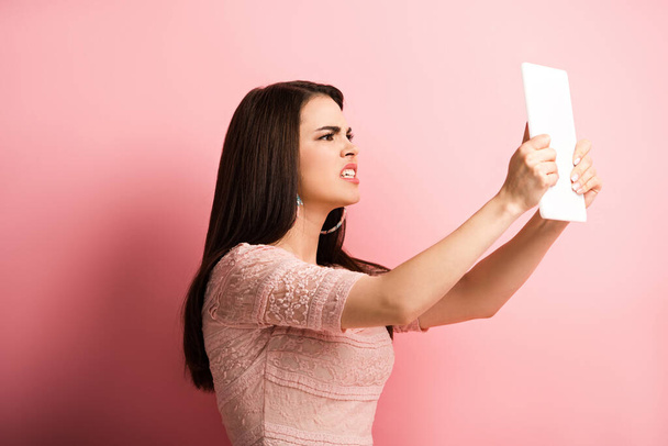 angry girl looking at digital tablet on pink background - Foto, Imagen
