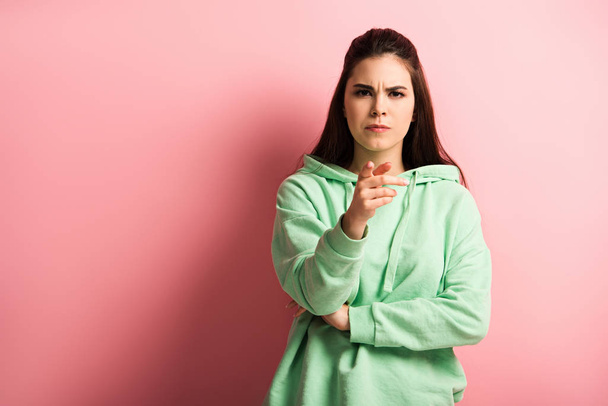 displeased girl pointing with finger while looking at camera on pink background - Photo, Image