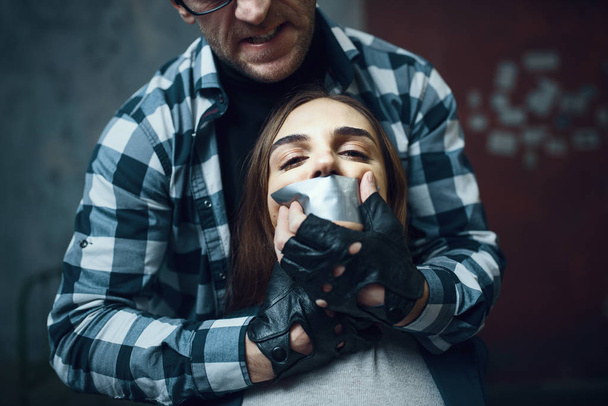 Maniac kidnapper tormenting his scared female victim. Kidnapping is a serious crime, crazy male psycho, kidnap horror, violence - Фото, зображення