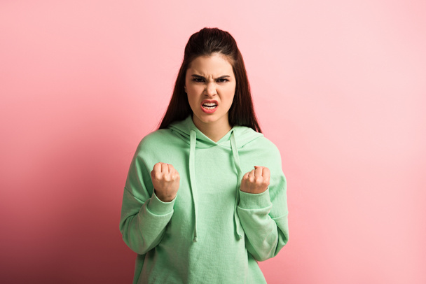 boos meisje tonen gebalde vuisten terwijl kijken naar camera op roze achtergrond - Foto, afbeelding