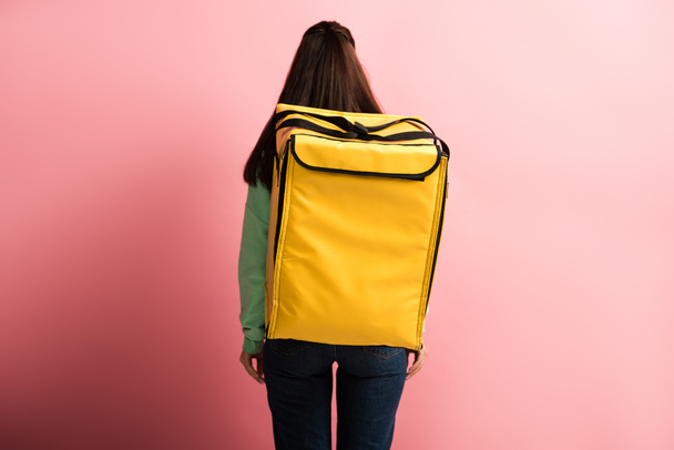 widok z tyłu kobieta przewożąca żółty termo plecak na różowym tle - Zdjęcie, obraz